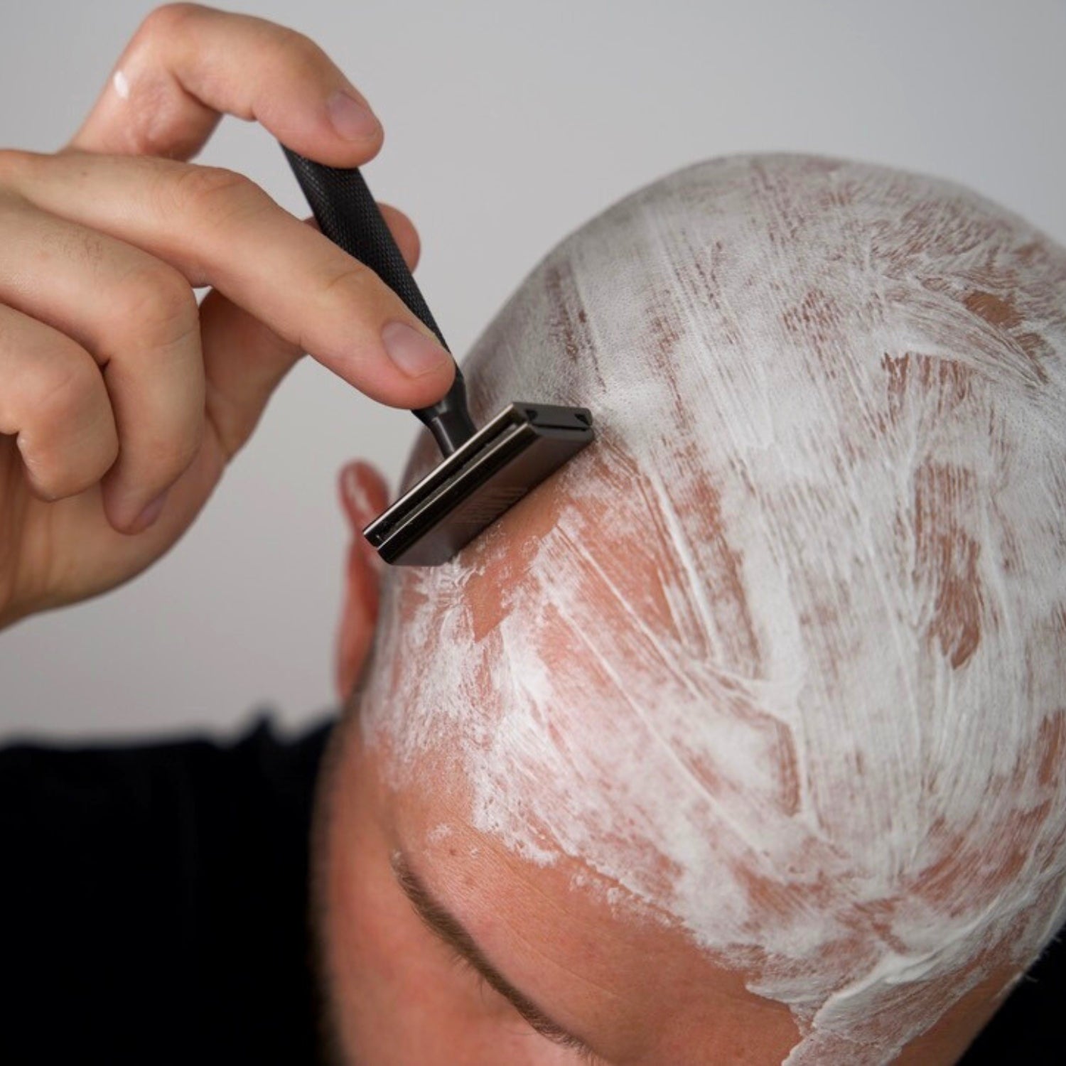 Mand barberer sit skaldede hoved med DE-Skraber og barberskum – traditionel vådbarbering for glat og tæt hovedbarbering